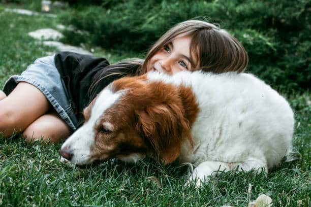 Chien et petite fille en train de jouer ensemble par terre dans le jardin